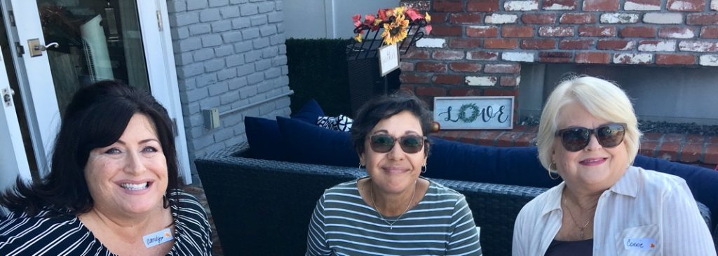 Three middle aged women sit together on a bench while smiling.