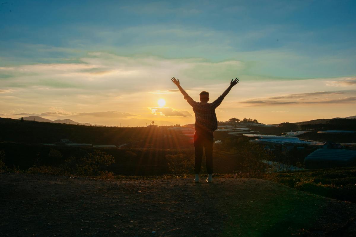 person watching the sun rise with their hands in the air