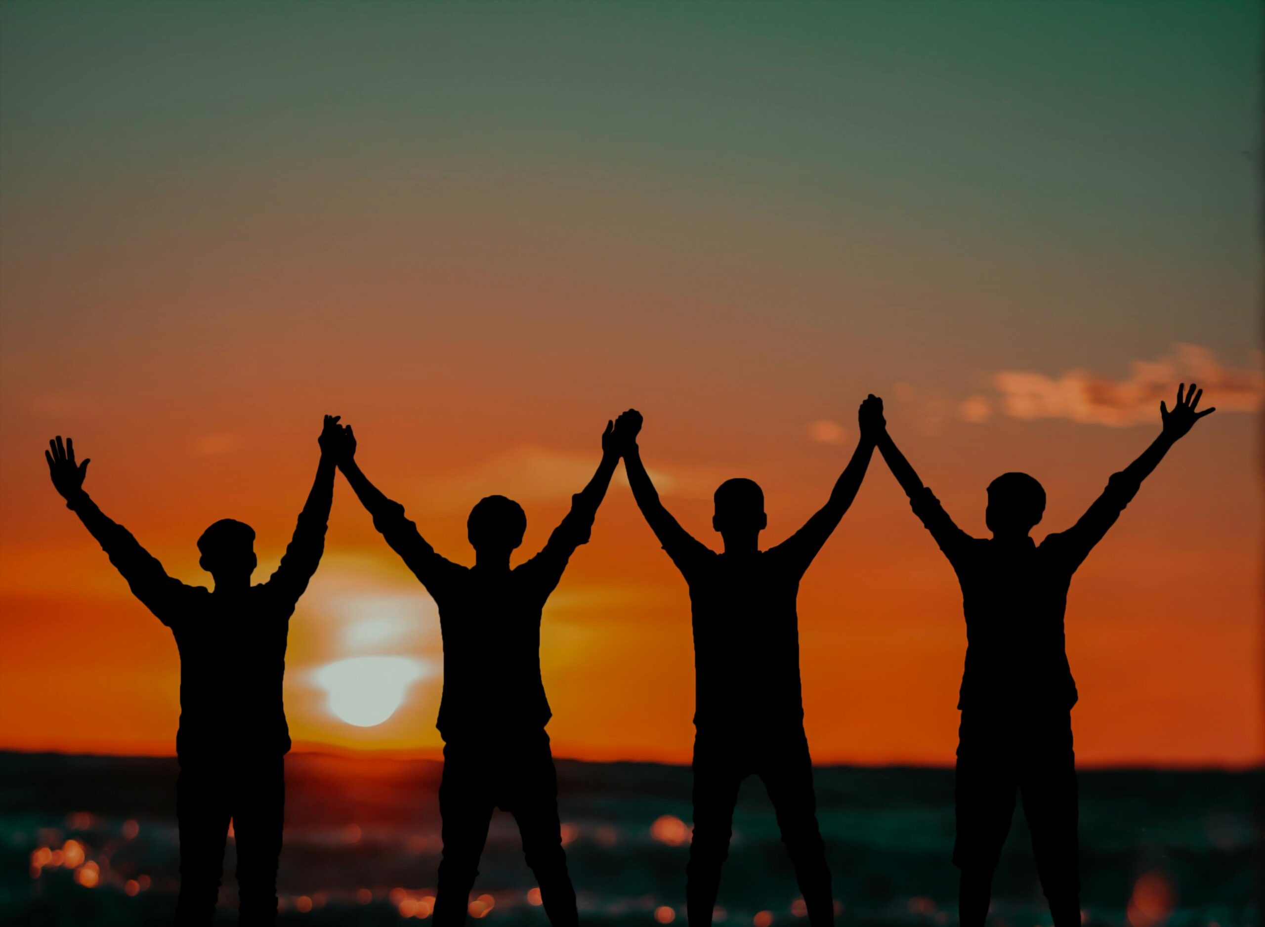 Silhouette of men raising their hands together at sunset.